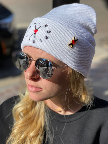 Woman wearing a white knit beanie with the circle of inspiration symbol embroidered on the fron and a 1