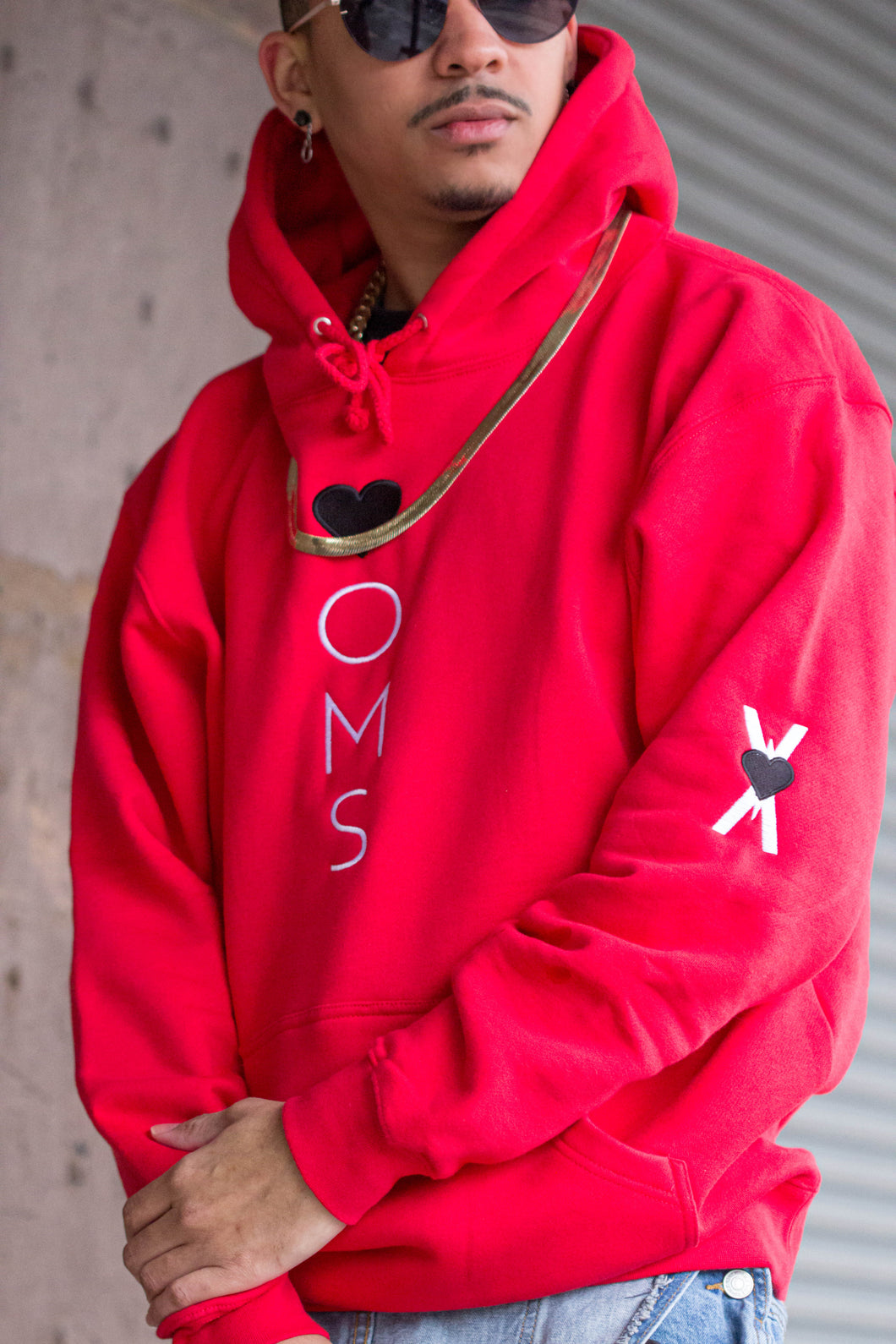 Man wearing red hoodie with heart-oms logo vertically embroidered down the front, and 